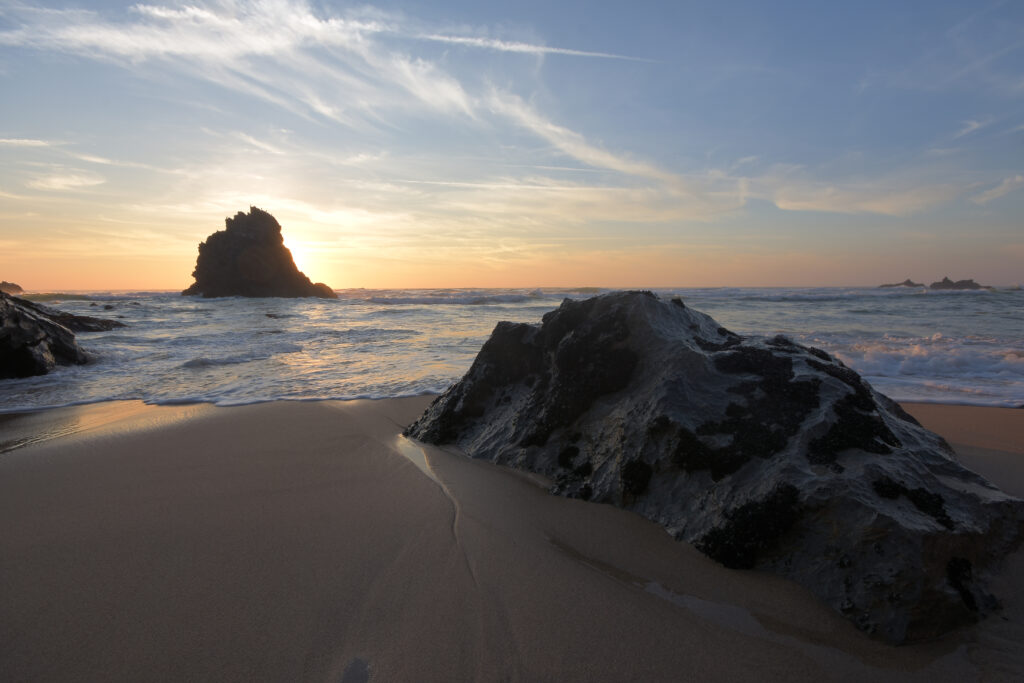 Sunset coastal wallpaper with rugged rocks waves sandy shore and golden sky silhouette peaceful view
