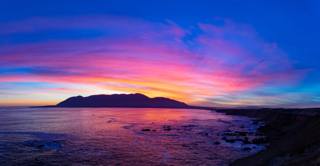 Sunset coastal wallpaper showing vibrant pink orange sky reflecting on sea with rugged coastline