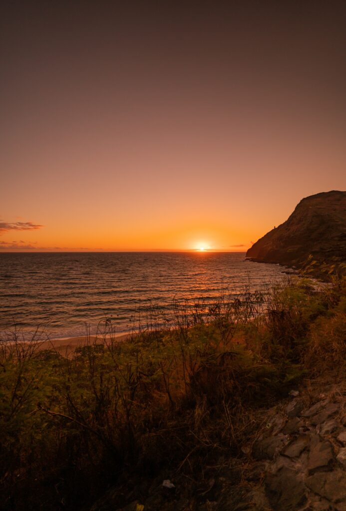 Sunset over rugged coastal cliff with golden sky and gentle waves on peaceful shore wallpaper