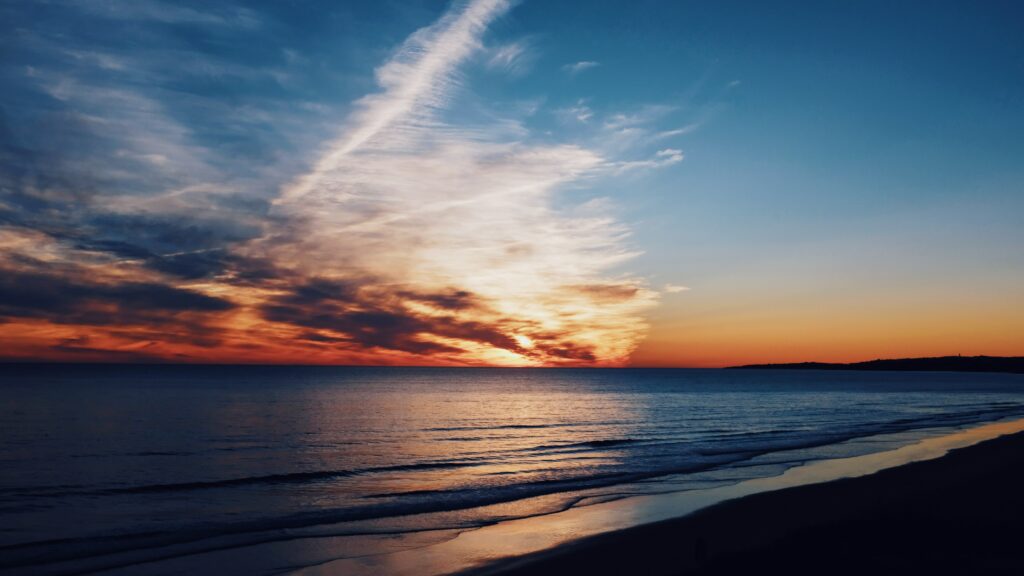 Sunset coastal scene with dramatic clouds glowing horizon and gentle waves on shore wallpaper
