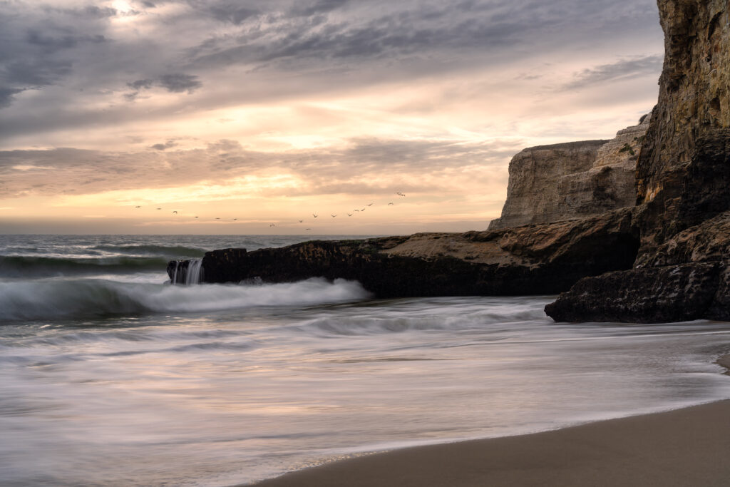 Sunset coastal wallpaper with pastel skies gentle waves rocky shoreline and distant flying birds