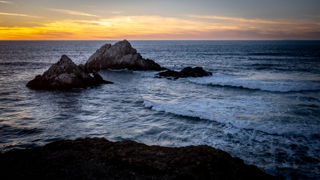 Rocky sea formations at sunset with gentle waves and golden coastal landscape wallpaper background
