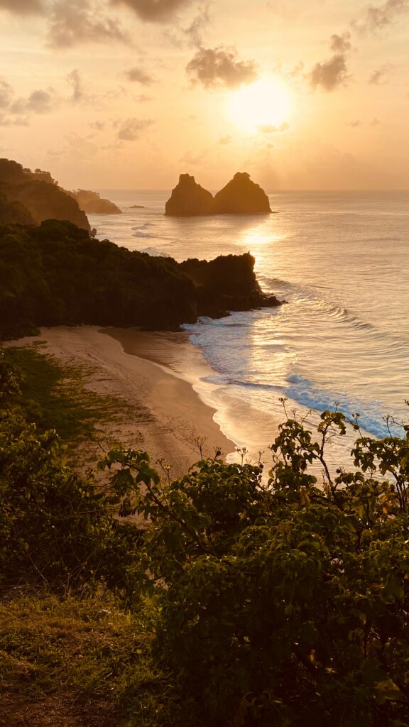 Sunset coastal wallpaper with golden waves rugged rocks green cliffs and a secluded sandy beach