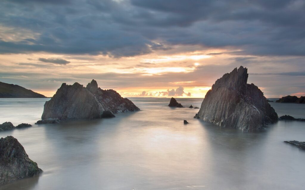 Jagged coastal rocks at sunset with warm light misty evening sea serene wallpaper background