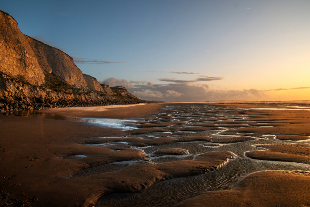 Serene coastal sunset with rippled sand shallow pools rugged rocks and golden light wallpaper