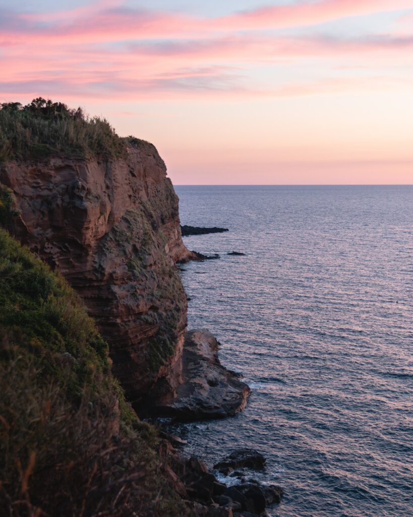 Serene coastal cliffs at sunset with pink purple sky overlooking calm sea rocky landscape wallpaper