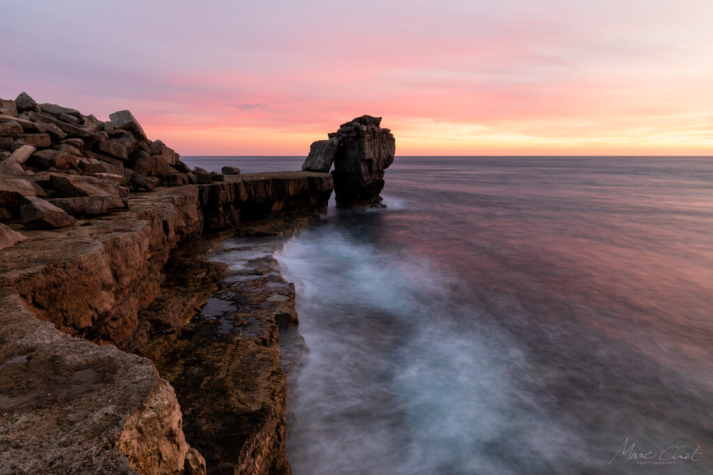 Sunset coastal scene with rugged rocks calm sea gentle waves glowing pink orange gold sky wallpaper