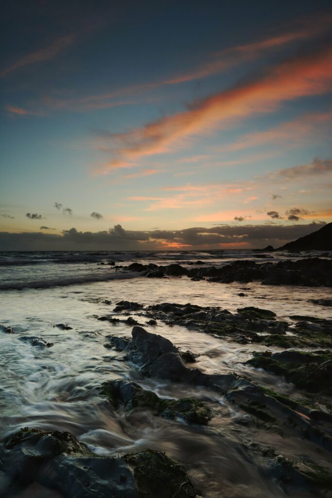 Serene coastal wallpaper with rugged rocks smooth stones sunset waves colorful twilight sky