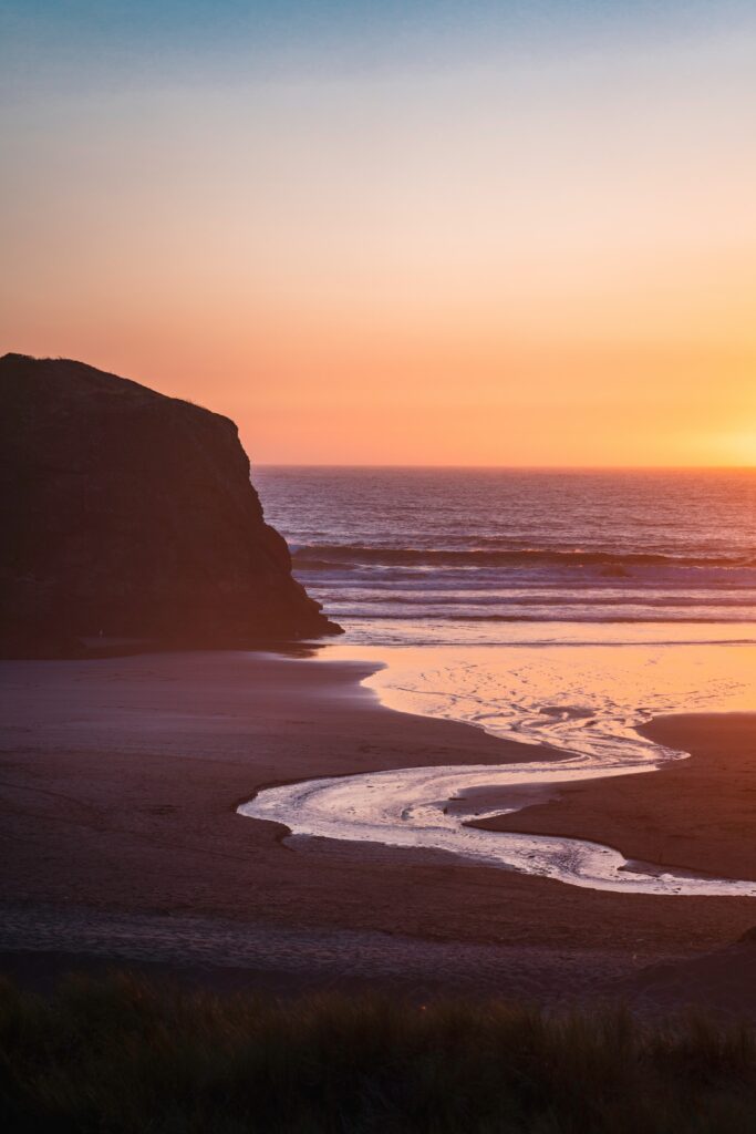 Serene coastal sunset with rugged rocks gentle waves orange purple sky reflecting on wet sand wallpaper