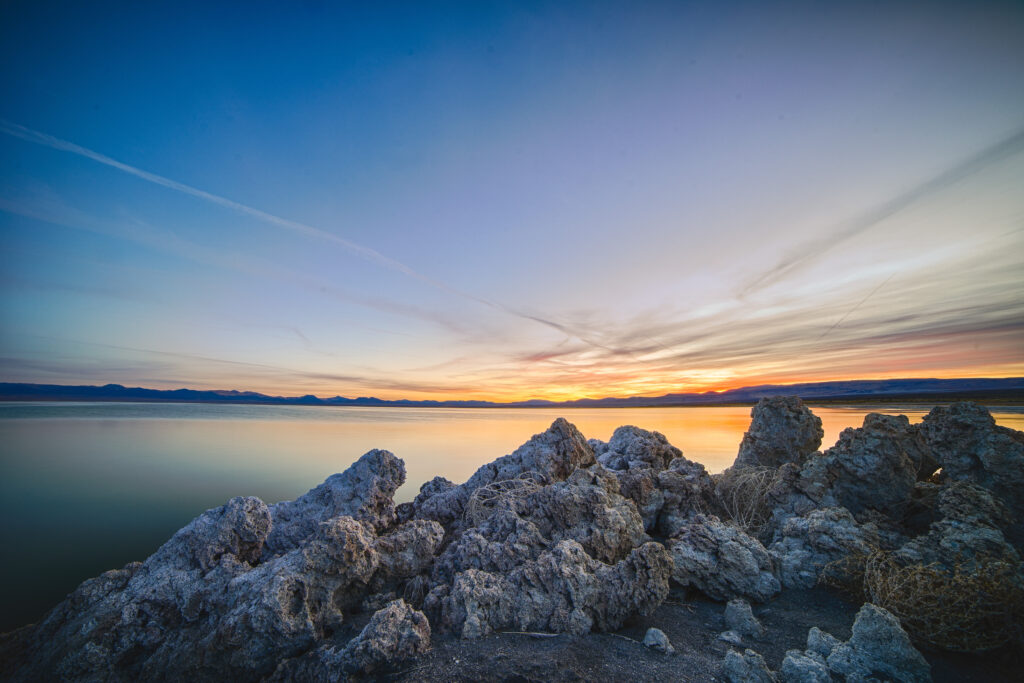 Tranquil sea with rugged rocks and vibrant sunset horizon coastal landscape wallpaper background