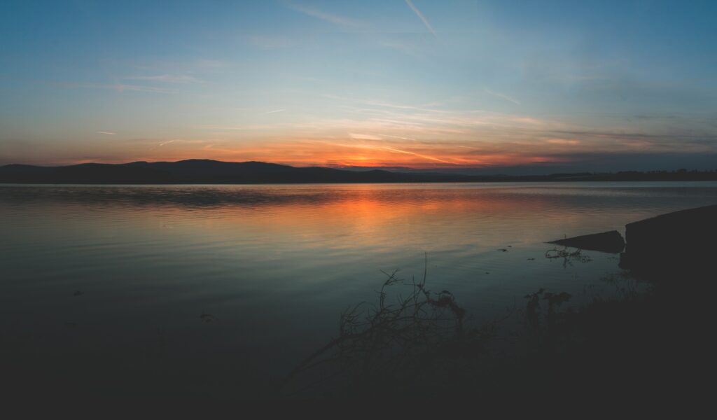 Serene coastal sunset wallpaper with orange blue sky silhouettes and calm water reflections