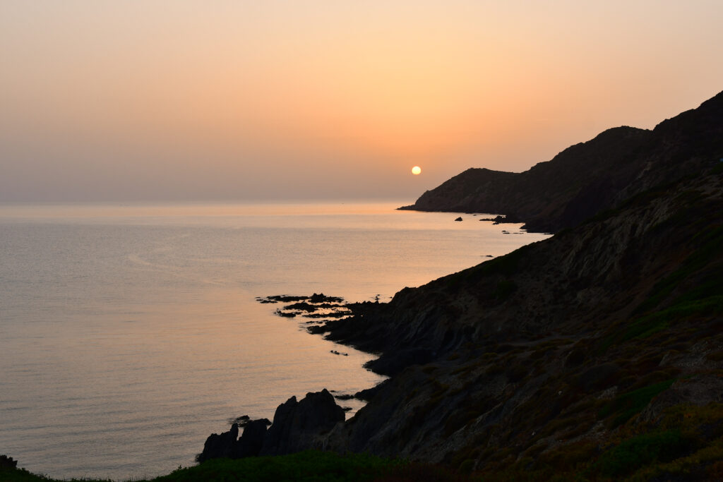 Serene coastal twilight with rugged rocks gentle waves and warm orange sunset wallpaper background