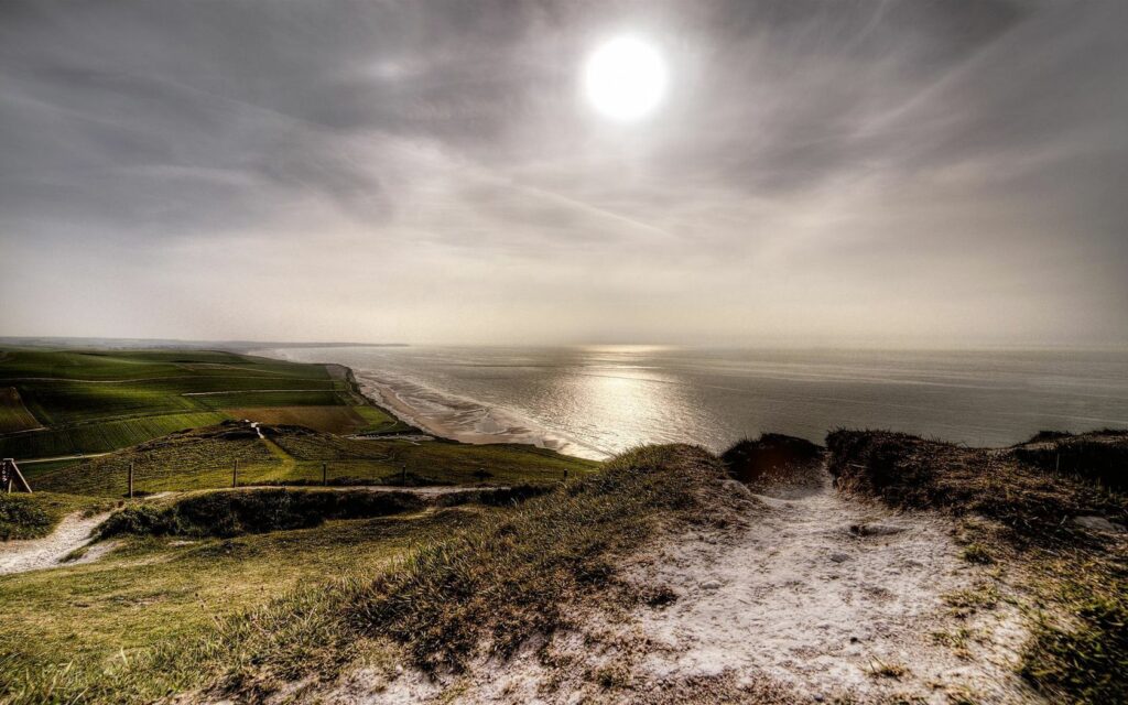 Coastal viewpoint with green fields cliffs and shimmering sea under bright sun serene landscape Wallpaper