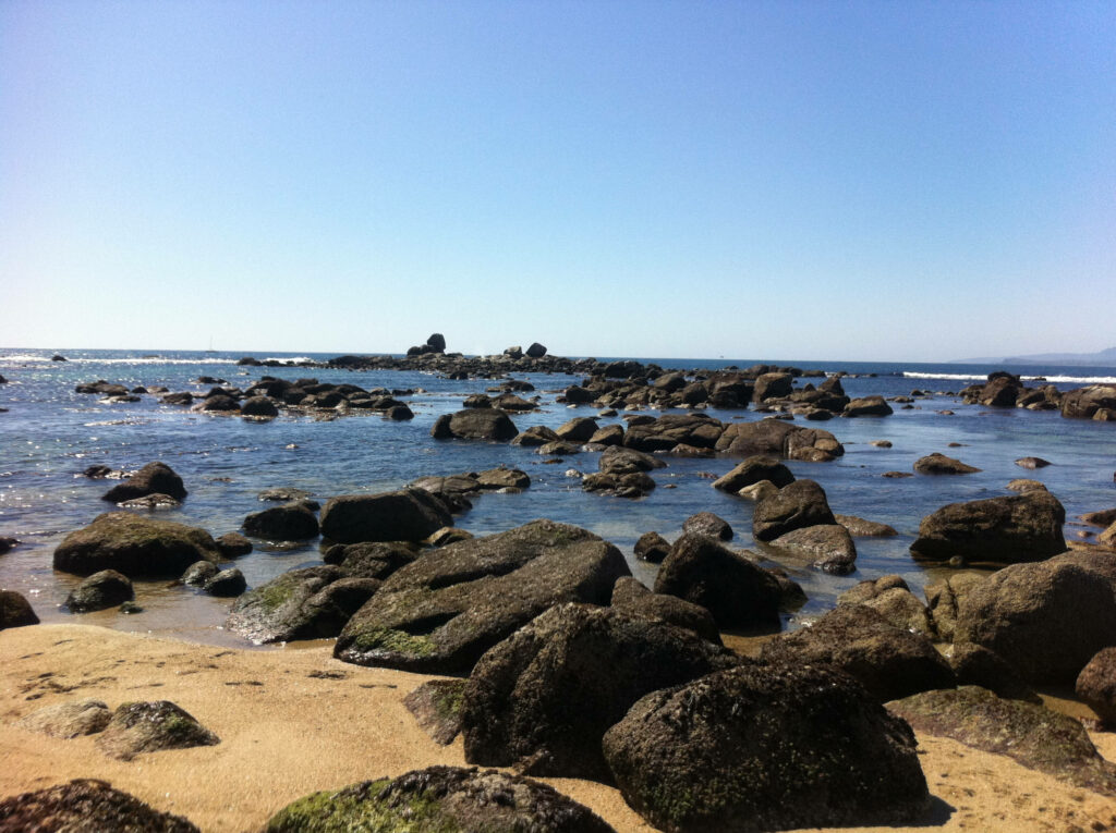 Serene Coastal Wallpaper: Black Rocks & Sandy Beach Under Blue Sky