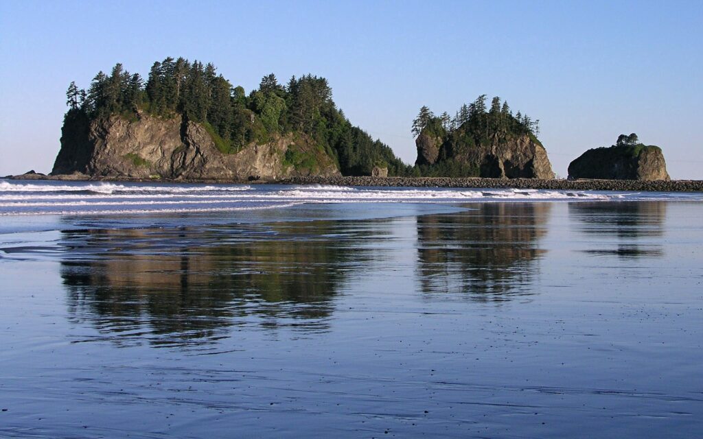 Serene coastal wallpaper with rugged islands rocky shore calm waves and lush green trees under blue sky