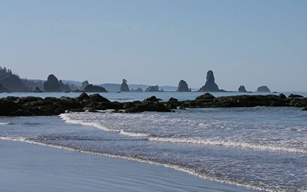 Serene coastal wallpaper with rugged rocks emerging from calm blue ocean waves under clear sky