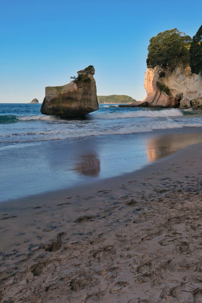 Rugged coastal rocks and tranquil beach with gentle waves under clear blue sky wallpaper background