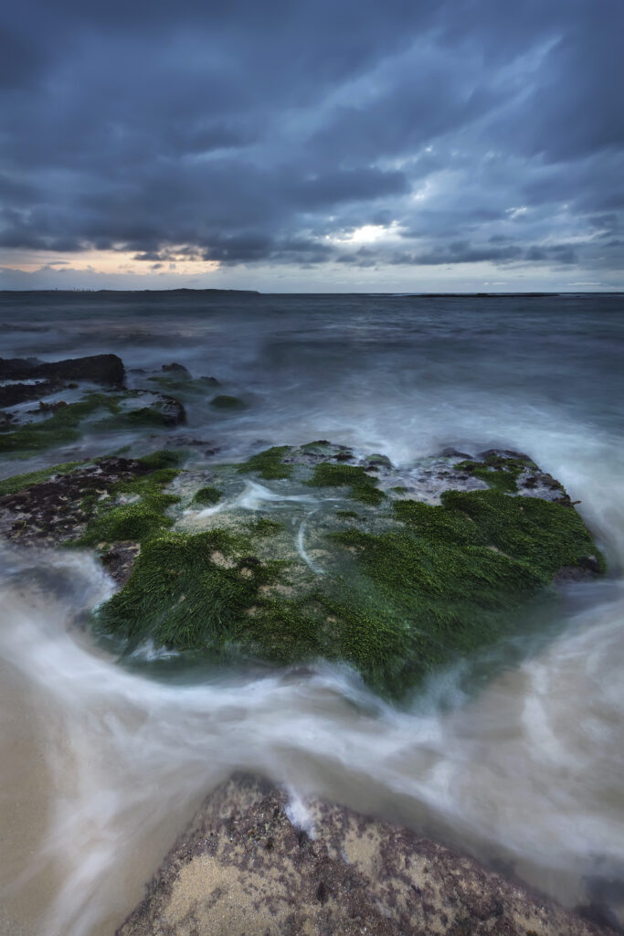 Coastal scene with mossy rocks swirling sea water dramatic cloudy sky blue green dusk wallpaper