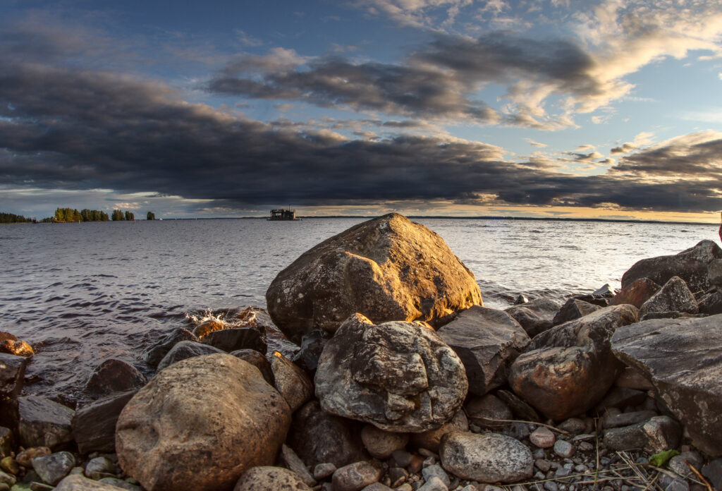 Serene coastal wallpaper with rough stones calm sea small boat dramatic cloud sky sunlight