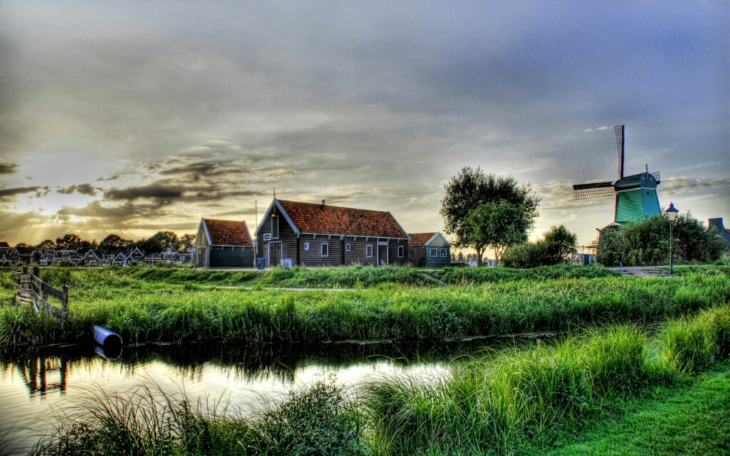 Peaceful village wallpaper with rustic farmhouses windmill lush green grass and gentle river reflection