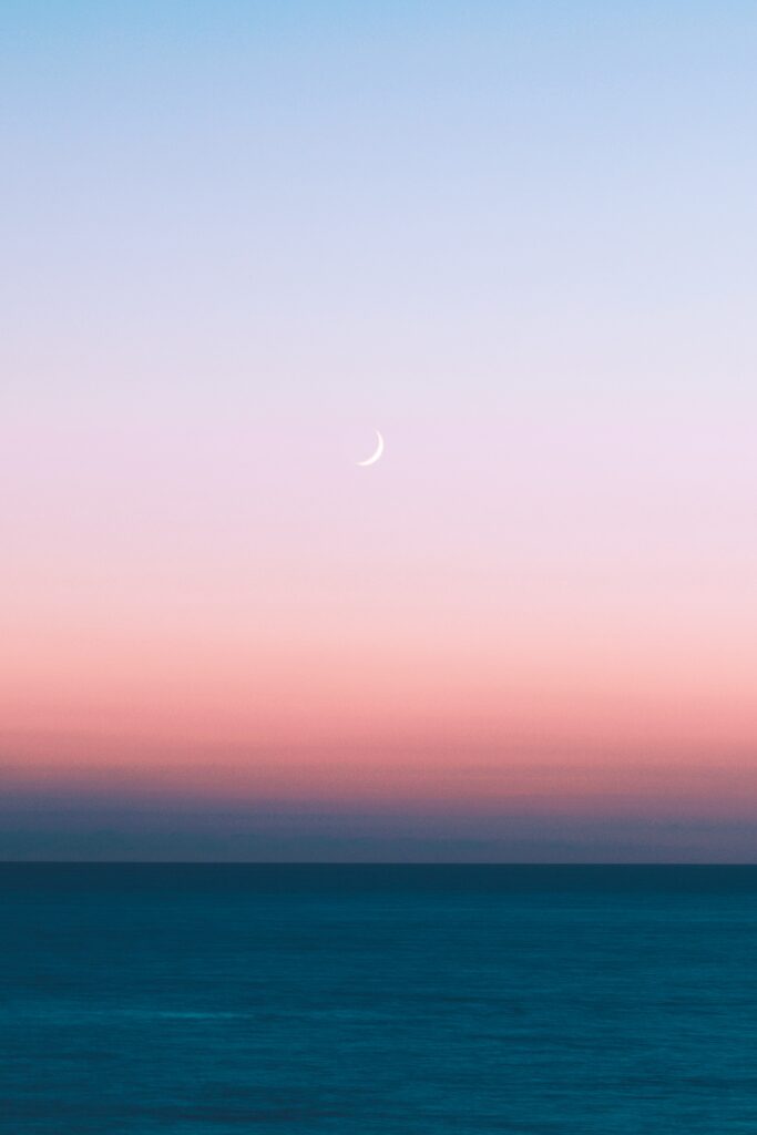 Crescent moon over calm sea at pink and blue sunset minimalist twilight wallpaper background