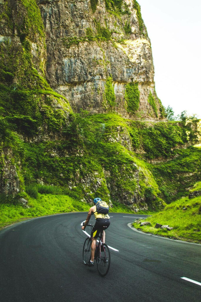 Serene Wallpaper: Cyclist on Winding Road Amidst Lush Green Cliffs