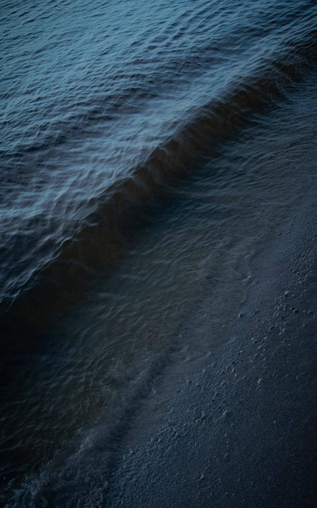 Serene dark mode wallpaper of calm seashore waves on textured sand at twilight minimalist background