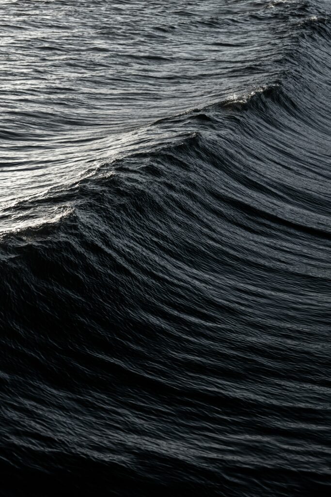 Dark ocean waves with intricate ripples and soft glare creating a serene wavy texture wallpaper