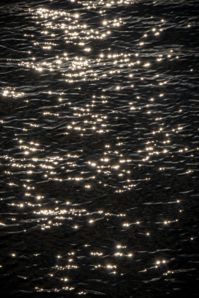 Serene dark water wallpaper with gentle waves glimmering under soft sunlight reflections