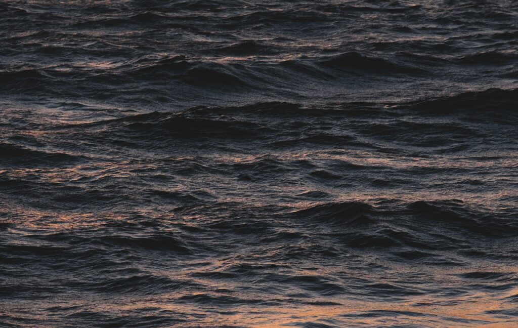 Serene deep blue sea waves reflecting golden light with textured surface natural wallpaper background