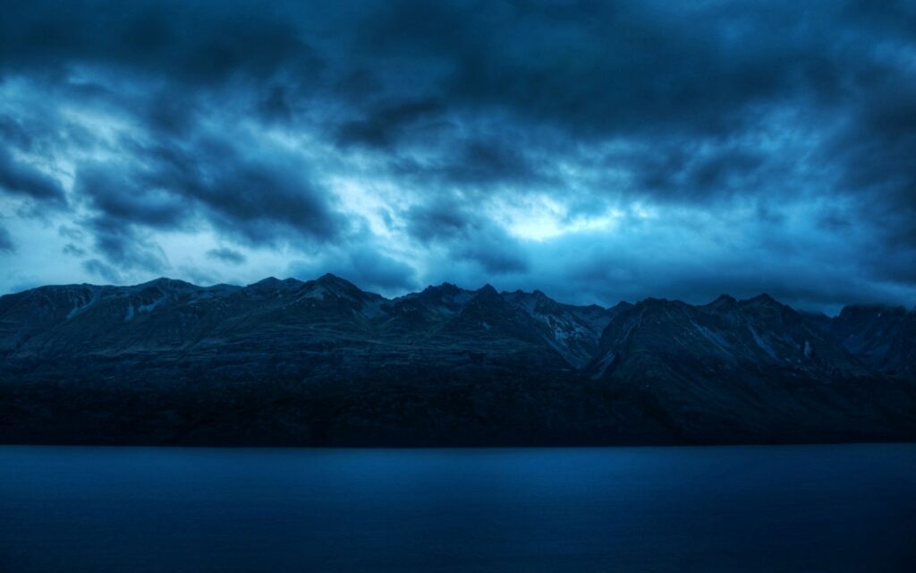 Mesmerizing wallpaper of deep blue water rugged mountains dramatic moody clouds serene nature