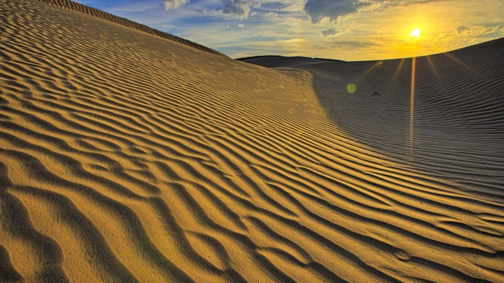 Serene desert dunes with golden sand ripples glowing under a radiant sunset sky wallpaper background