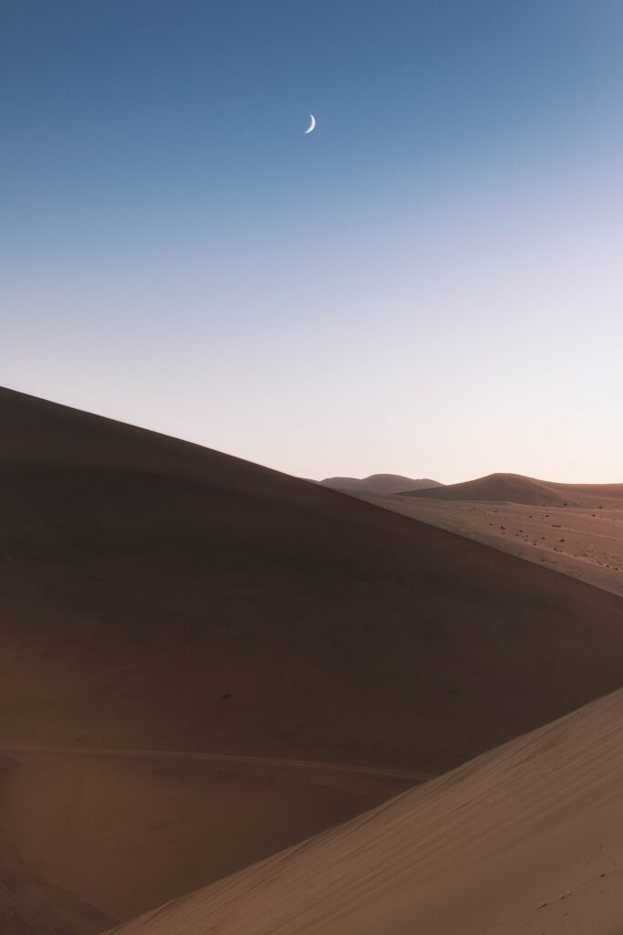 Serene desert wallpaper with golden sand dunes crescent moon and twilight blue sky background