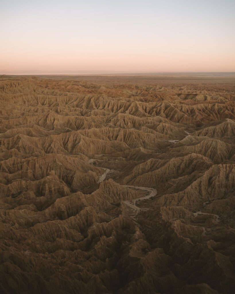 Expansive desert landscape with eroded ridges and pastel horizon in warm earthy tones wallpaper
