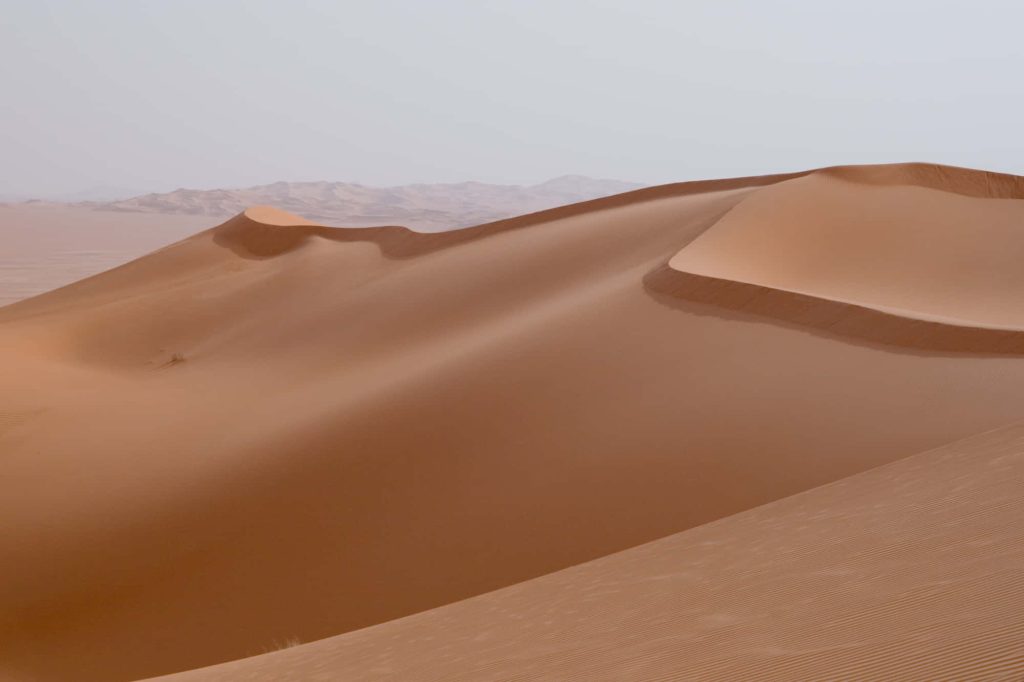 Vast rolling sand dunes with warm orange hues in serene desert landscape wallpaper background