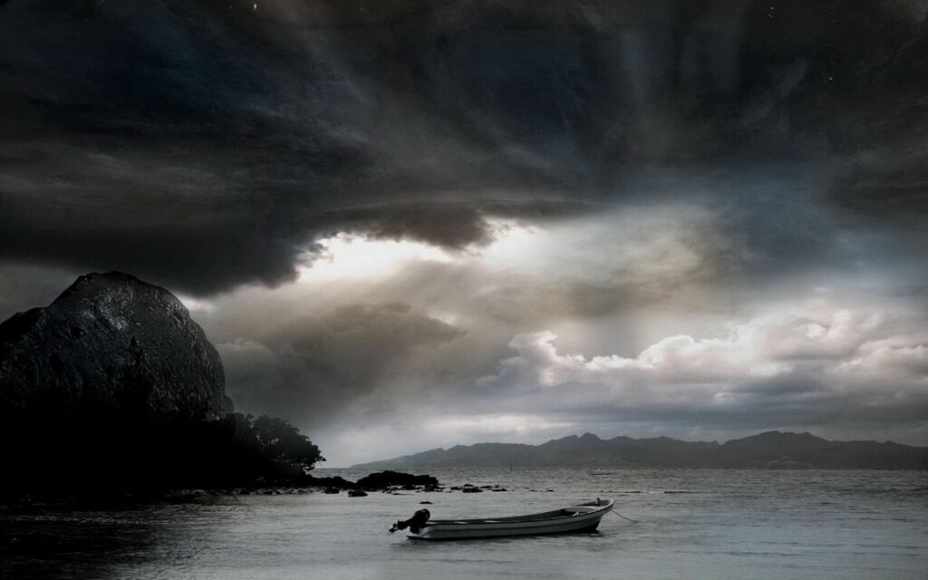 Solitary boat on calm sea under dramatic cloudy sky with soft light over distant mountains wallpaper