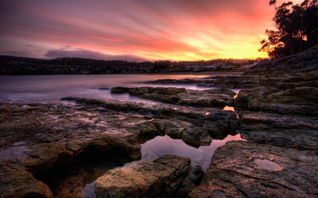 Evening coastal scene with rugged stone formations calm water and vibrant sunset sky reflection Wallpaper