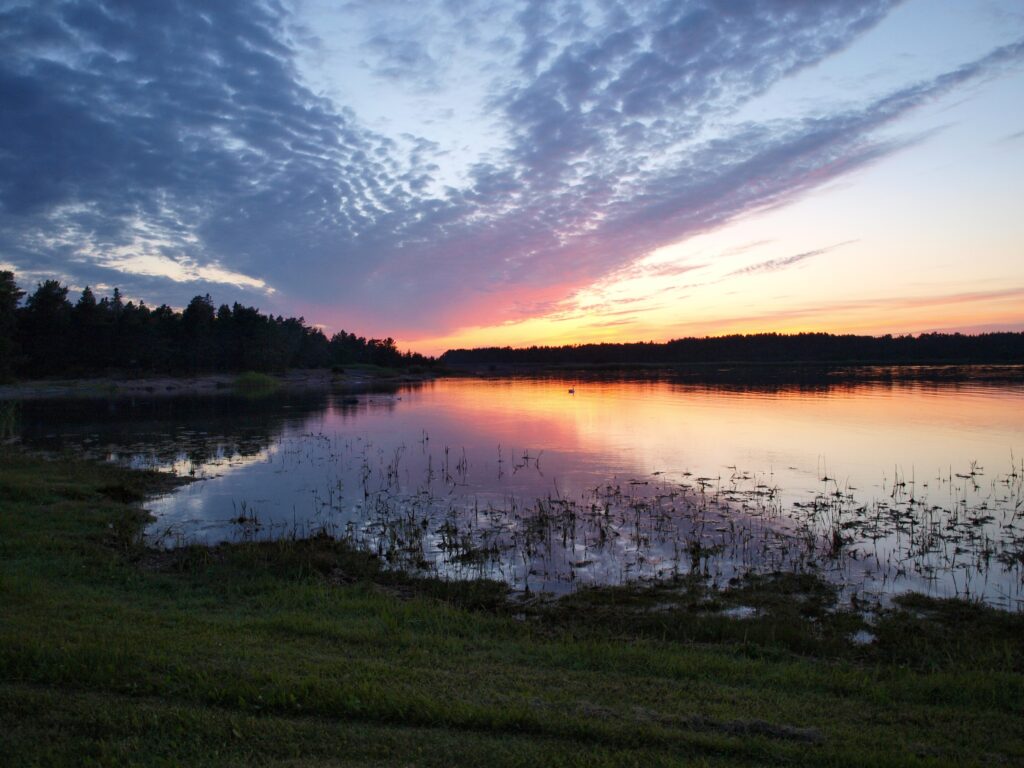 Serene evening lake with orange purple sky and dramatic clouds reflecting on calm water surface Wallpaper
