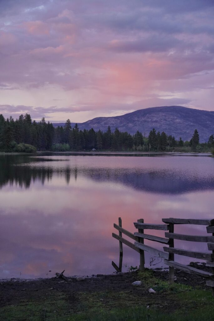 Serene evening lake reflecting pastel dusk sky with distant forest mountain and rustic wooden fence Wallpaper