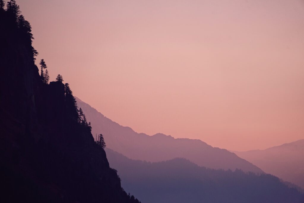 Serene evening landscape with rugged rock cliffs pine tree silhouettes and layered mountains Wallpaper