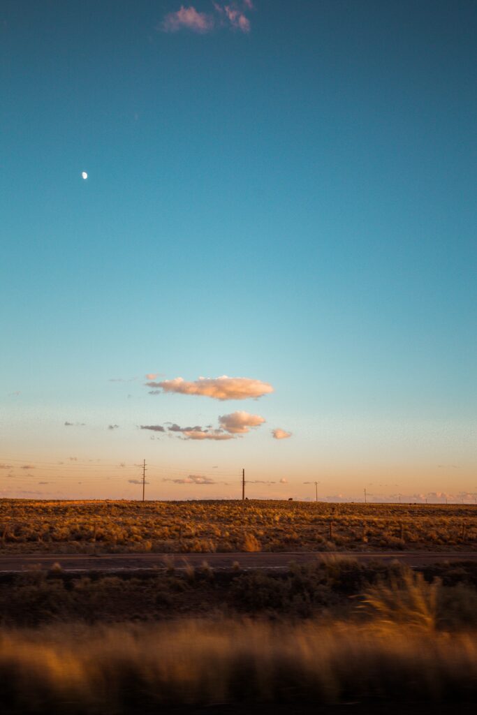 Serene evening road beside open field under golden light with clear sky and sparse clouds wallpaper