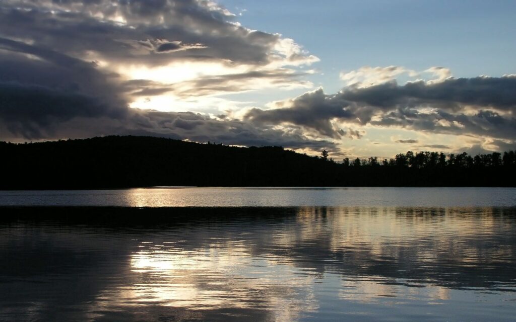 Serene evening sea wallpaper with dramatic clouds silhouetted trees and calm water reflections