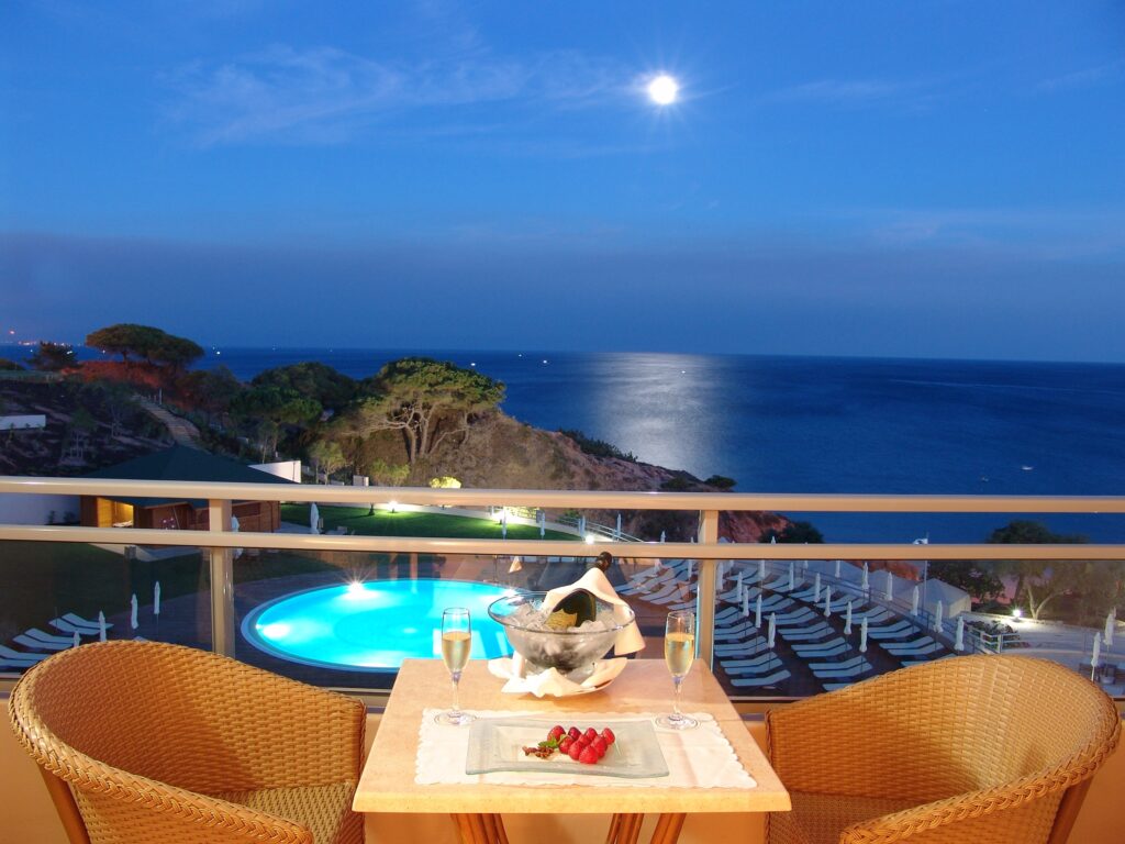 Cozy candlelit dinner on balcony by tranquil pool lush greenery and calm ocean at moonlit night Wallpaper