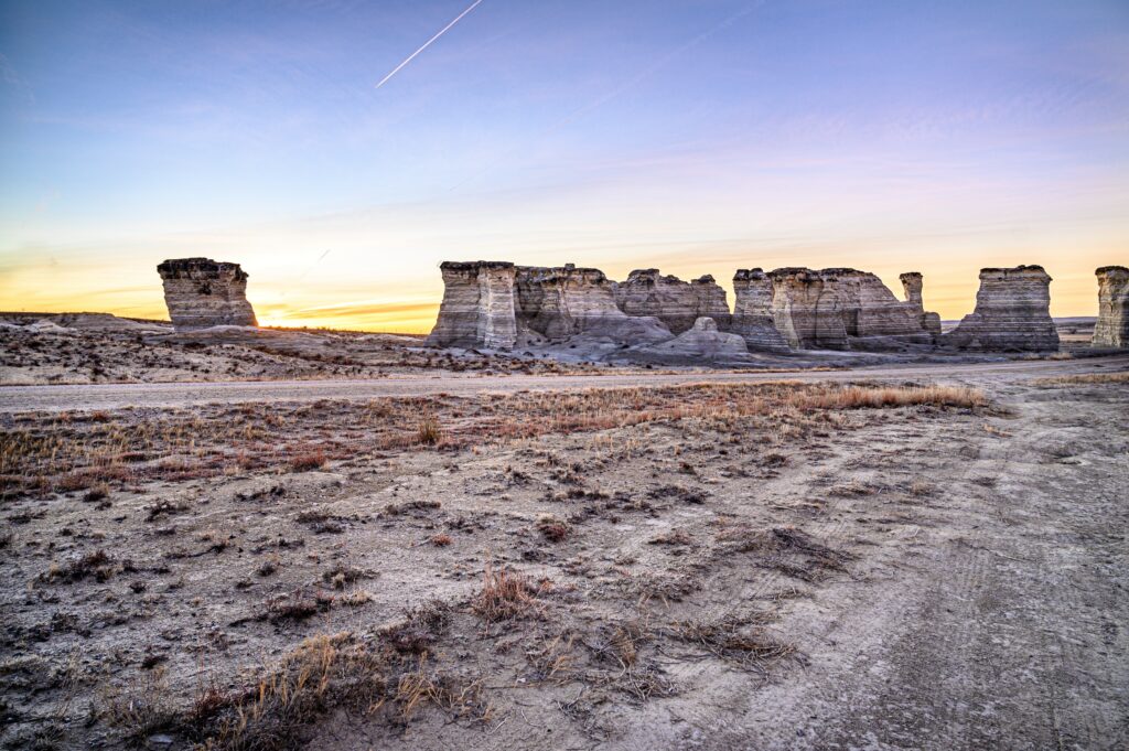 Evening sunset over rugged stone formations with pastel purple blue gold sky and sparse vegetation Wallpaper