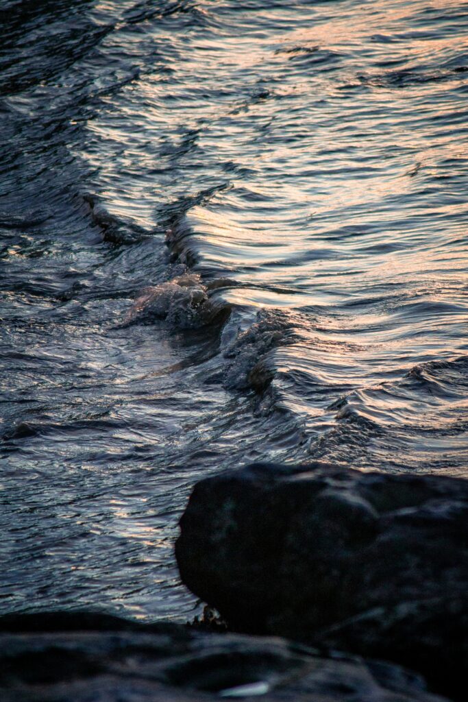 Gentle waves and water spray shimmer over textured stream with dark rocks in foreground wallpaper