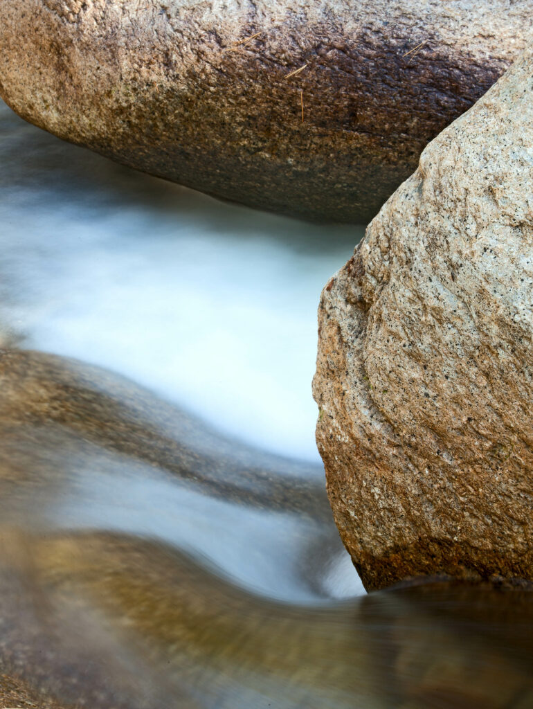 Long exposure of smooth water flowing between textured stones creating a serene nature scene Wallpaper
