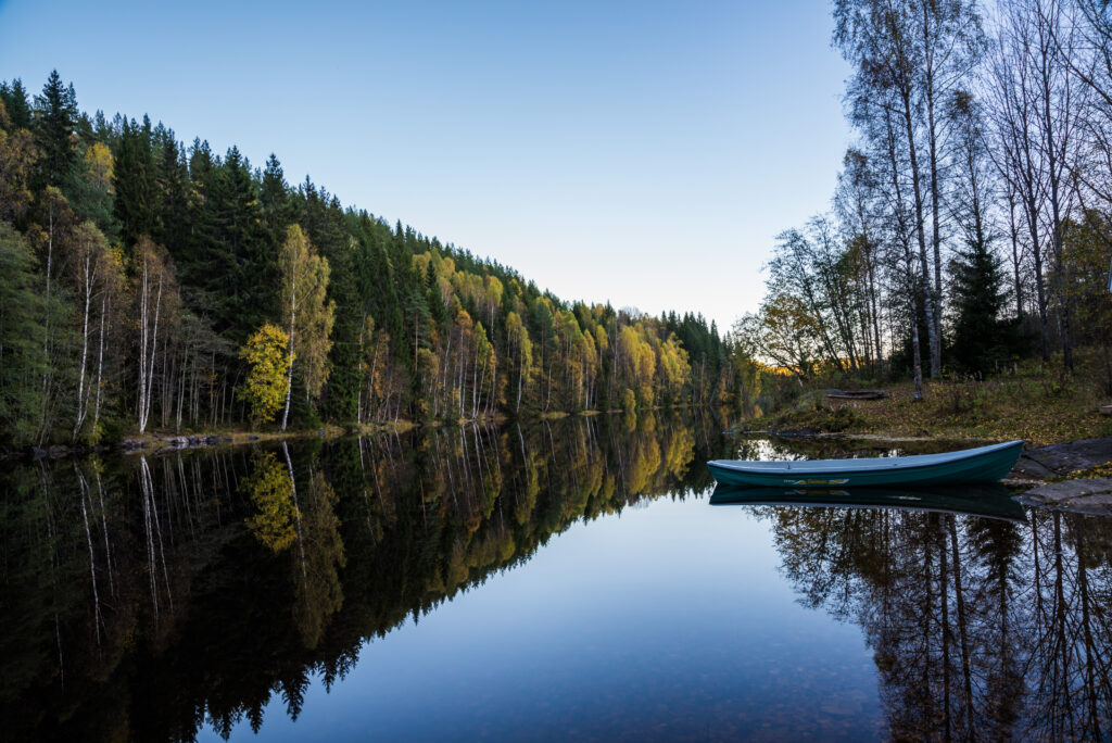Tranquil river in lush forest with colorful trees clear sky and small boat on serene shore Wallpaper