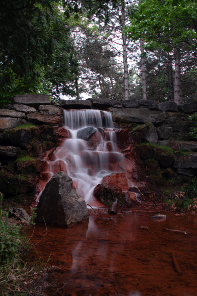 Serene forest landscape with gentle waterfall cascading over mossy stones and lush greenery Wallpaper