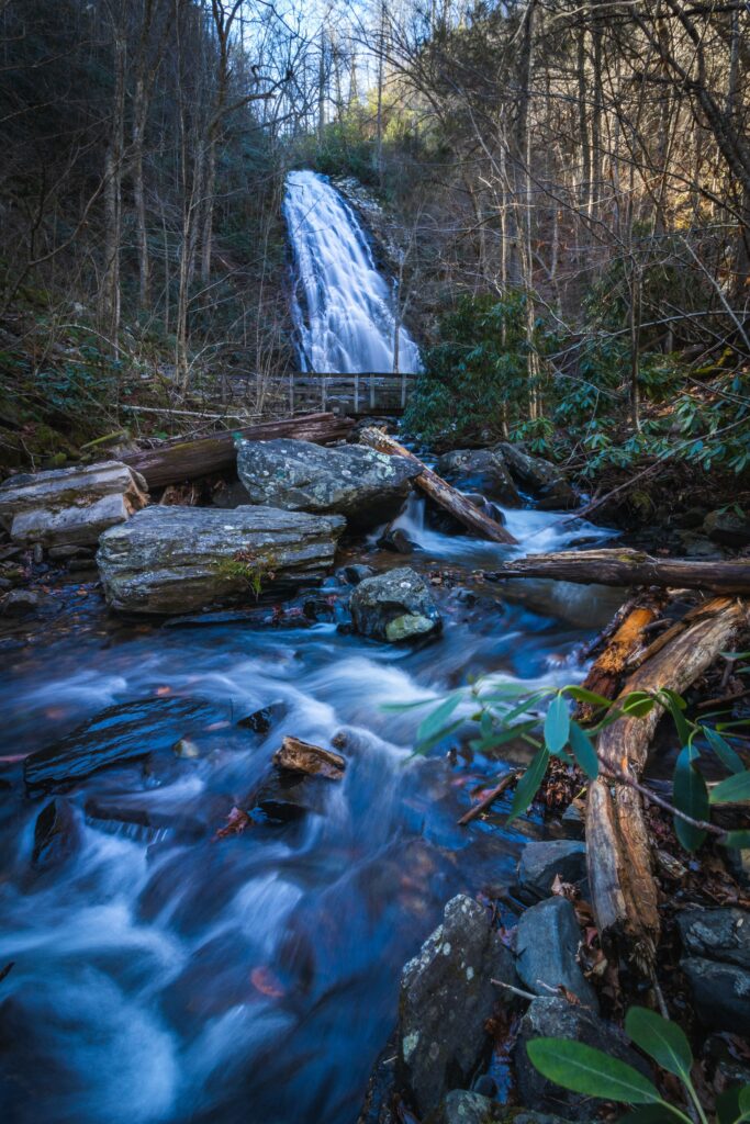 Tranquil waterfall flowing over rocky cliff into river surrounded by mossy stones and lush trees Wallpaper