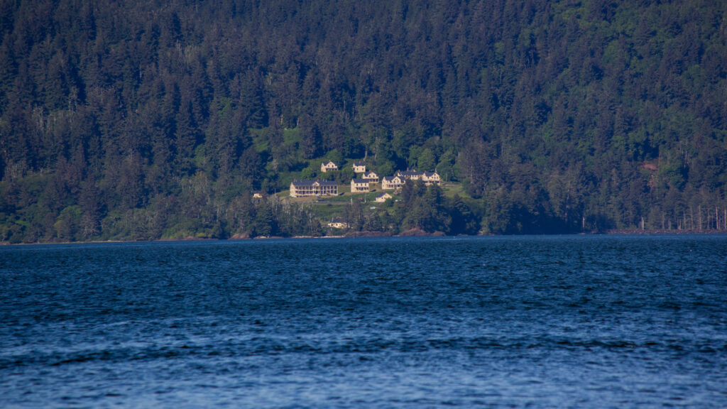 Grand manor and forested hillside overlooking tranquil blue water under clear sky wallpaper background